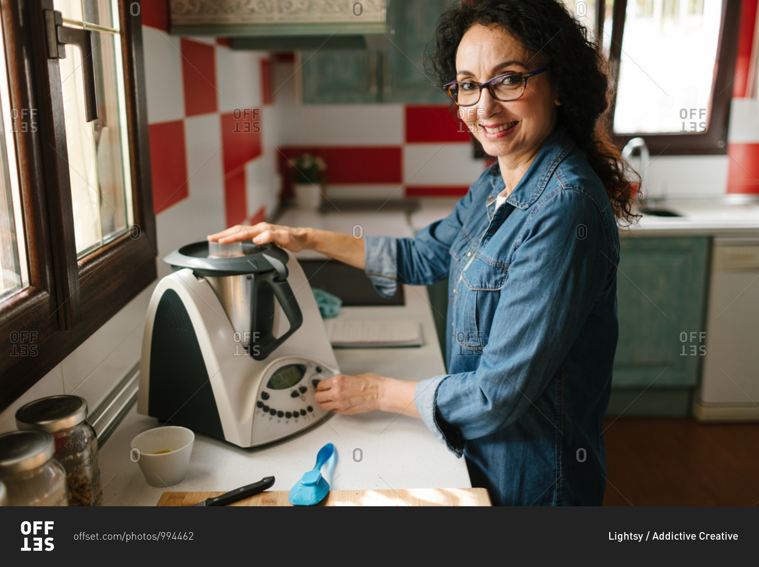Smiley middle-aged woman cooking with a kitchen robot