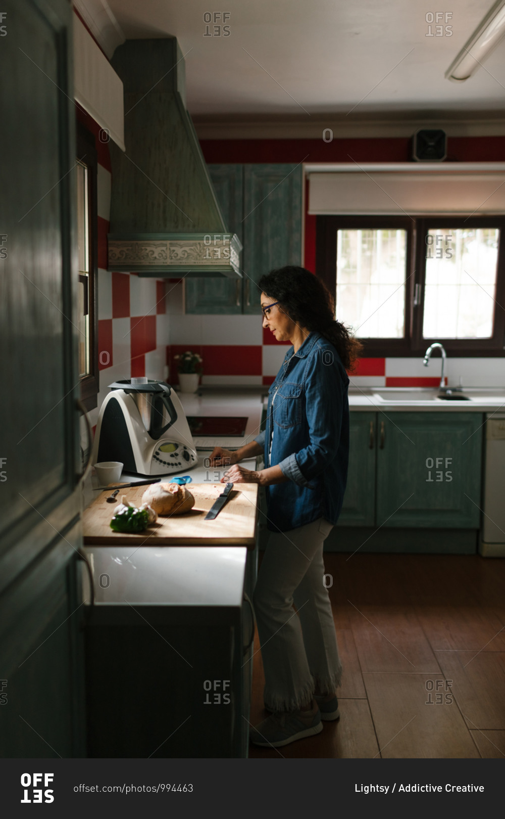 A middle-aged woman is waiting the recipe to be ready because she is cooking with a kitchen robot