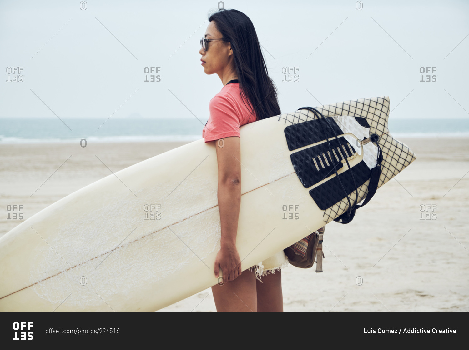 Side view of young Asian female surfer in summer outfit
walking on sandy beach and carrying surfboard against calm blue sea
looking away stock photo - OFFSET