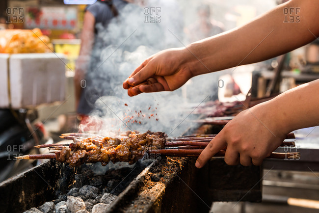 Side view of anonymous man seasoning meat on skewers while cooking delicious kebab in kitchen