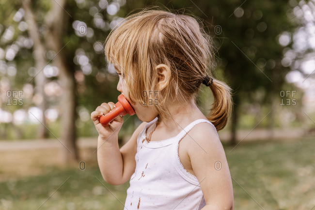Side view of adorable child standing with dirty mouth in park and eating yummy chocolate ice cream