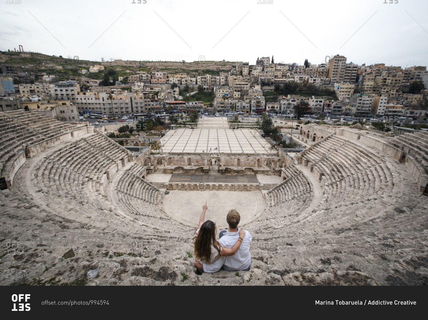 High angle back view of traveling couple sitting on stone stairs of ancient theater in Amman during summer holiday