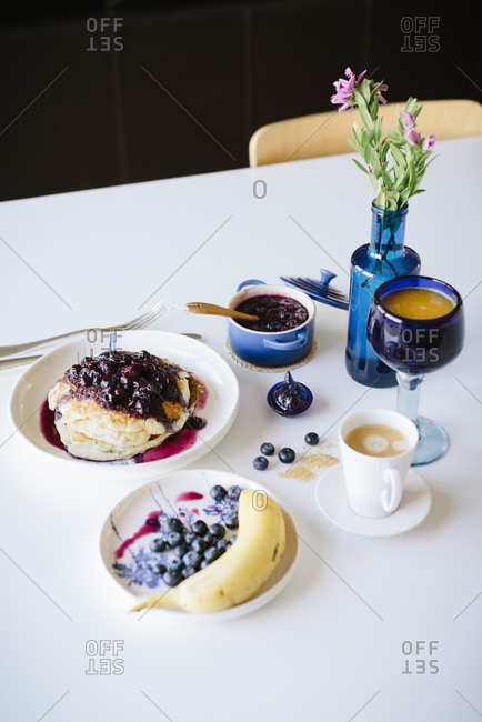 From above delicious homemade pancakes with blueberry jam served with cup of coffee and fresh berries and banana on table setting for home brunch in cozy kitchen