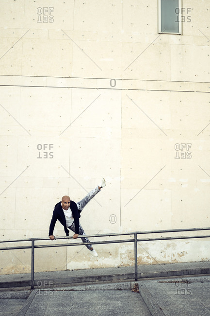 Flexible male in casual wear performing trick on metal railing while jumping and doing parkour