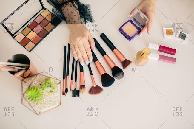 Crop makeup artist demonstrating various beauty products and accessories placed on table in beauty salon