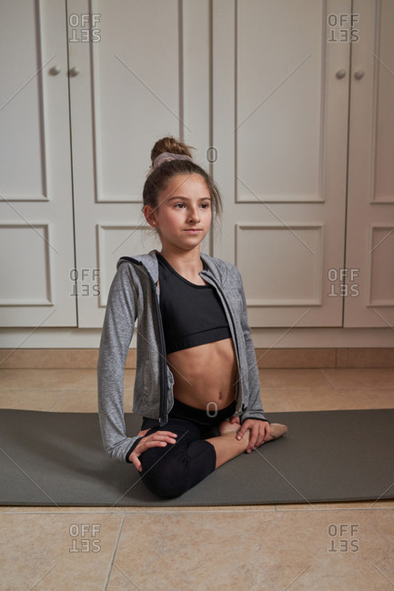From above slim teenage girl sitting on mat doing splits practicing gymnastics at home looking away