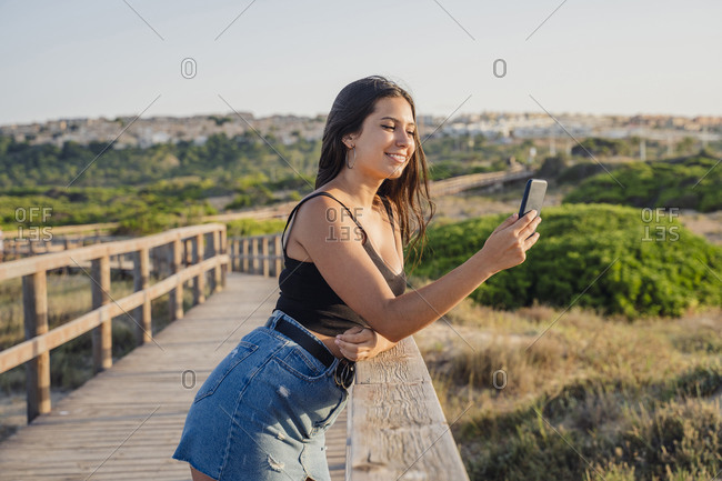 Teenage girl taking selfie through smart phone while standing on boardwalk at beach