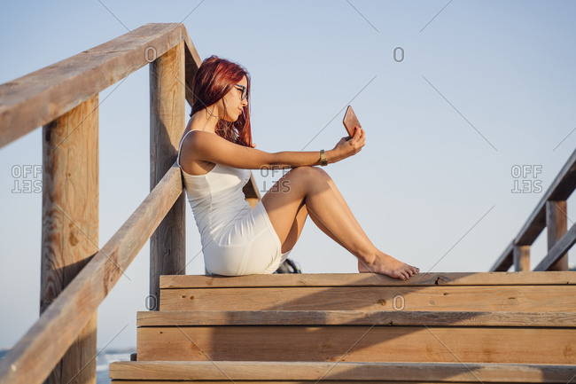 Teenage girl taking selfie through smart phone while sitting on wooden steps against clear sky