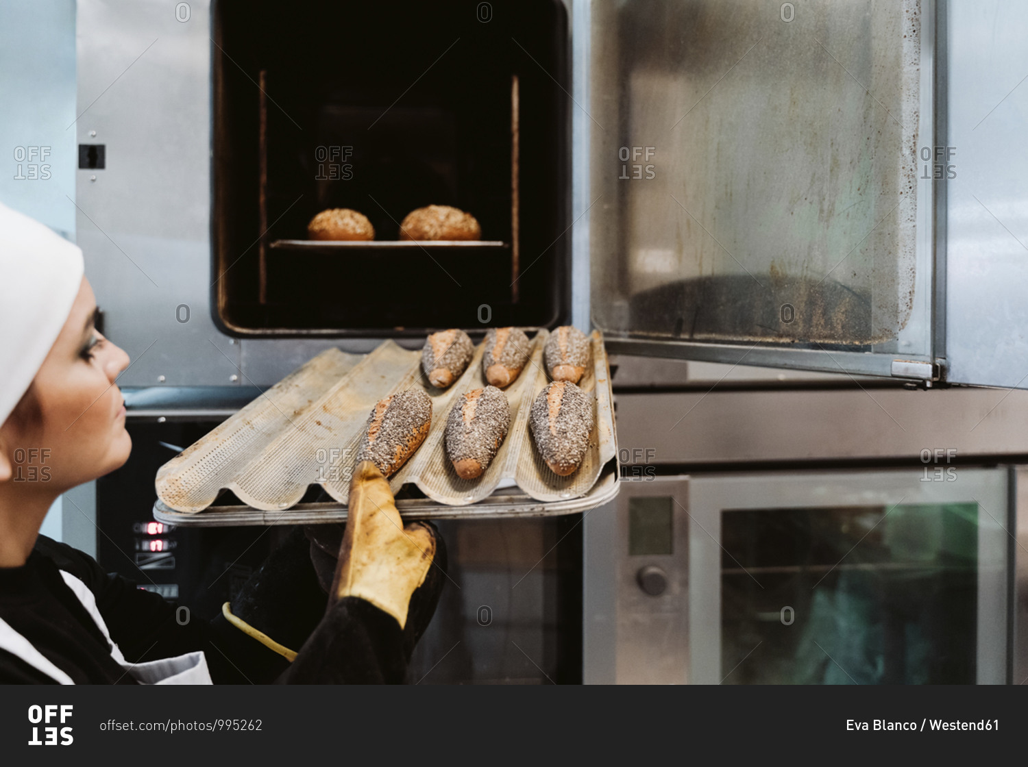 Female baker inserting wholegrain bread on baking pan in oven at bakery
