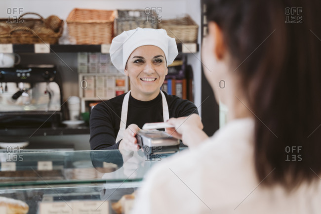 Happy female baker receiving contactless payment through credit card from customer at bakery