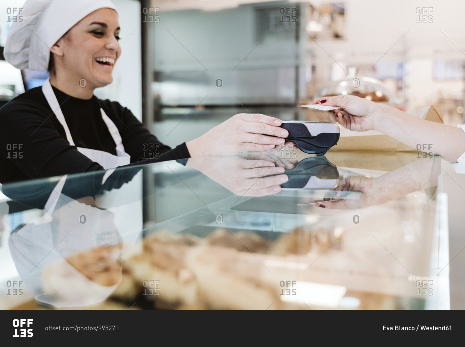 Happy baker receiving contactless payment through credit card from customer at bakery