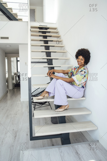Happy woman sitting on floating stairs in modern penthouse