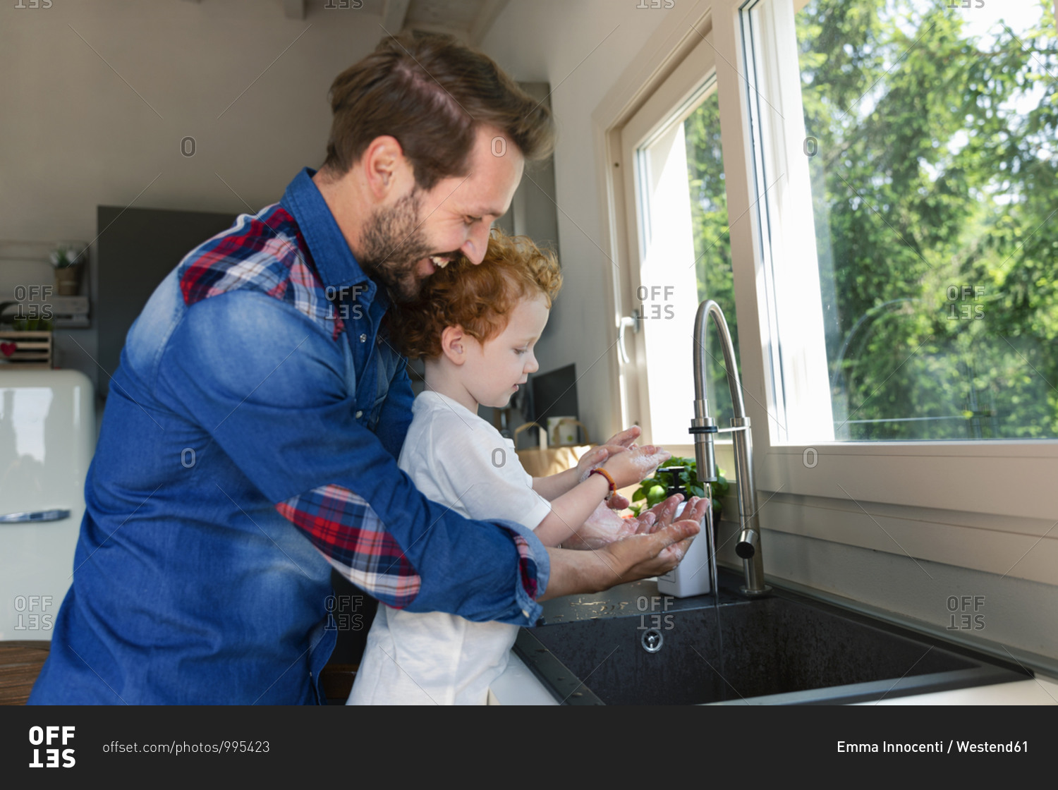 Smiling man washing hands with son in kitchen sink at home