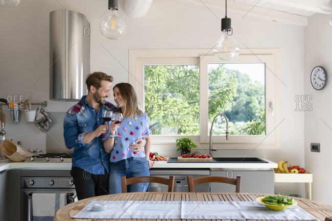 Happy mid adult couple enjoying wine while standing in kitchen at home