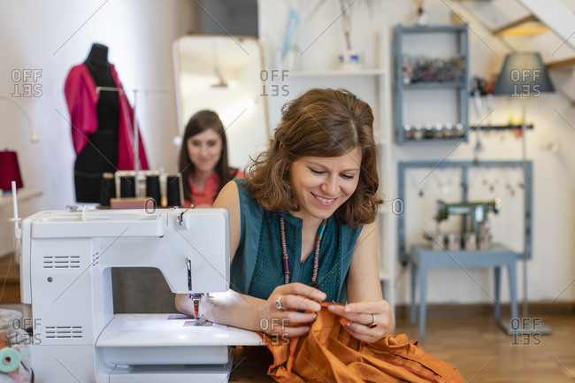 Smiling female tailor looking at fabric by sewing machine in design studio