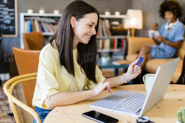 Happy woman using credit card and laptop while shopping online in cafe