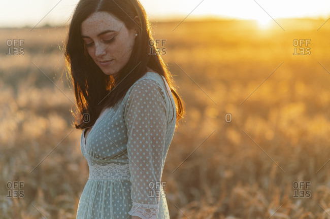 Thoughtful young woman looking down while standing in farm at sunset