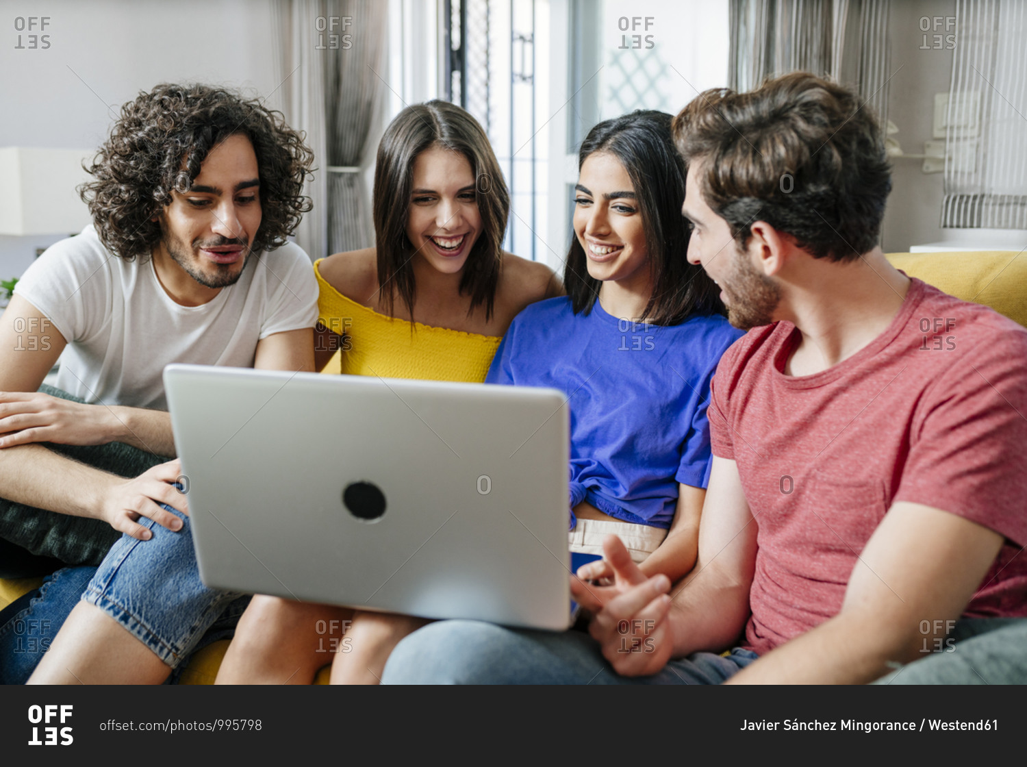 Smiling multi-ethnic friends sharing laptop while sitting in living room