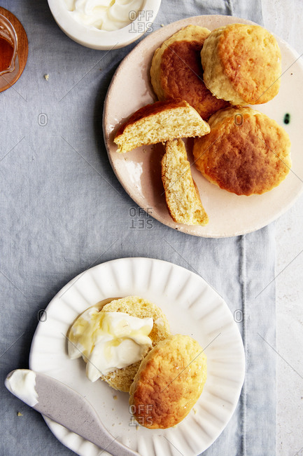 A plate of scones with honey and whipped cream on a linen tablecloth