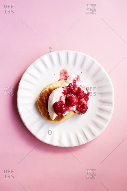 Scone with cream and raspberry coulis on a pink background