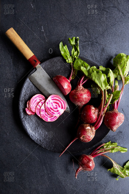 A bunch of candy stripe beetroot on a plate with one sliced on a dark moody background