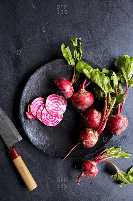 A bunch of candy stripe beetroot on a plate with one sliced on a dark moody background, top view