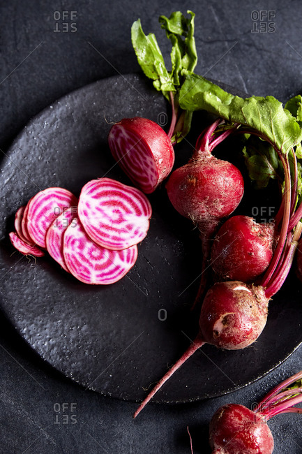 A bunch of candy stripe beetroot on a plate with one sliced on a dark moody background, close up