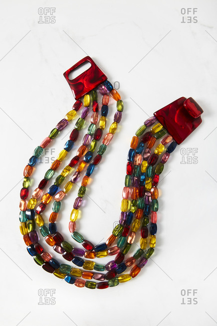 A multicolored beaded necklace with a red acrylic clasp necklace on white background