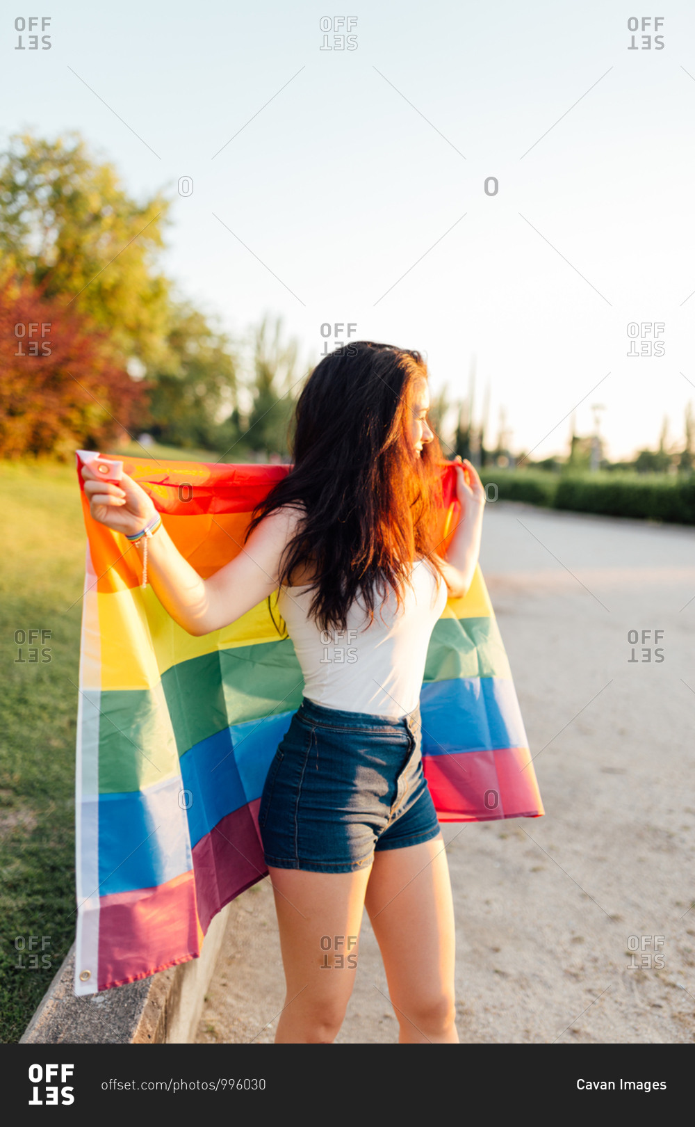 Young woman with the sun on her face with an lgtb flag on her back ...