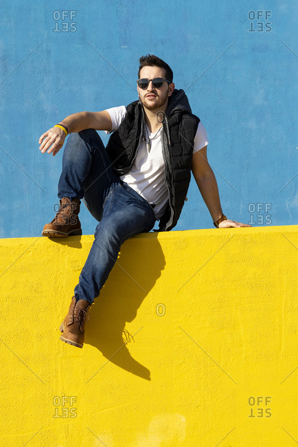 Bearded man in white t-shirt, jacket and jeans against blue background