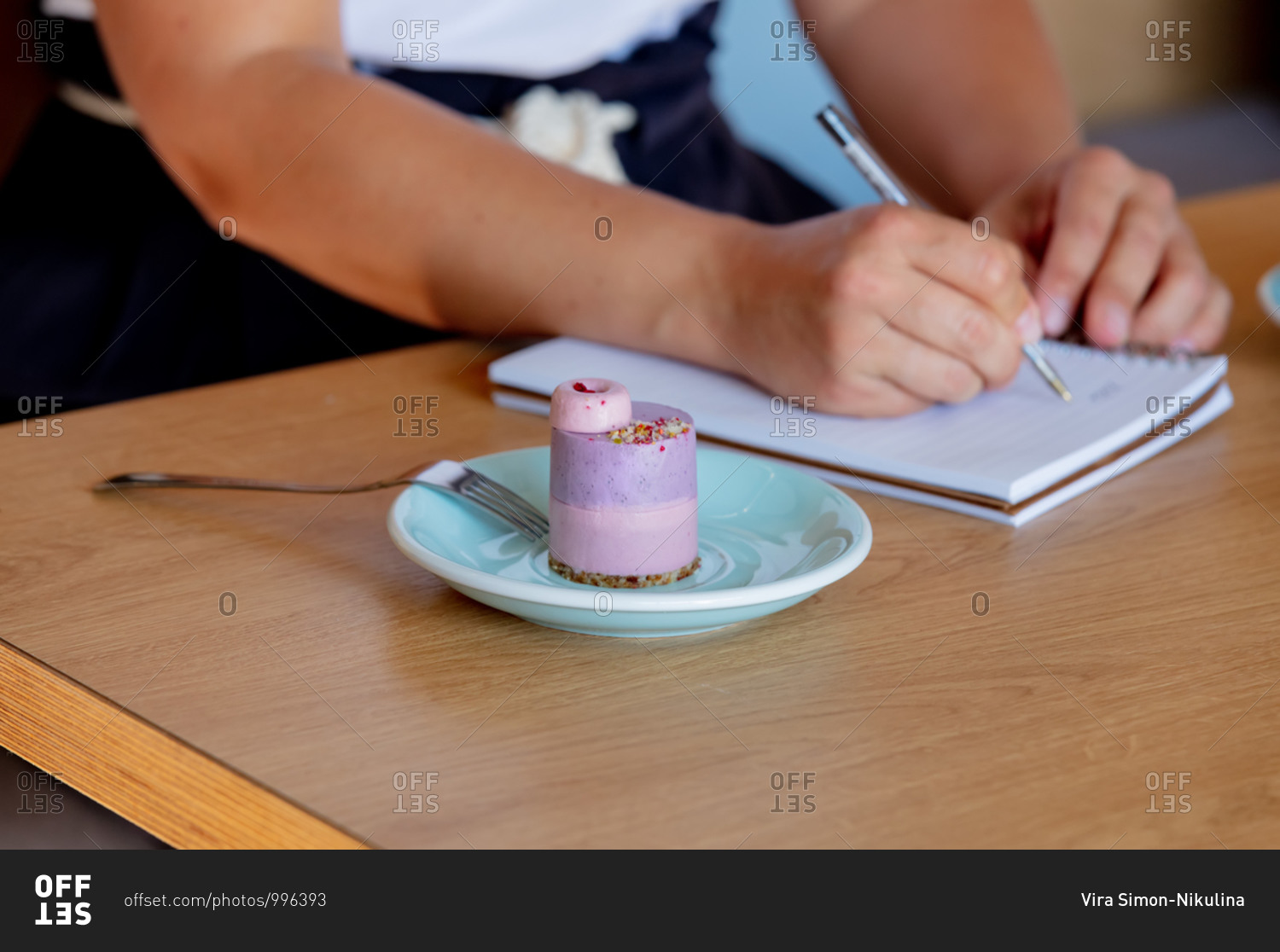 Woman writing in a notebook on a table in a cafe beside a gluten-free cake