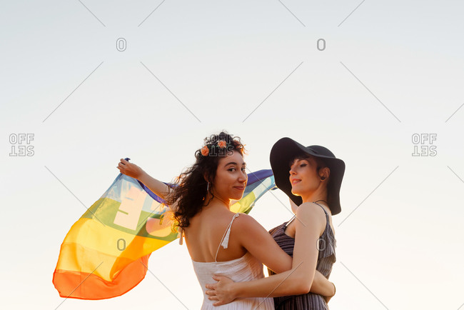 Happy women raising multicolored flag standing on sea beach