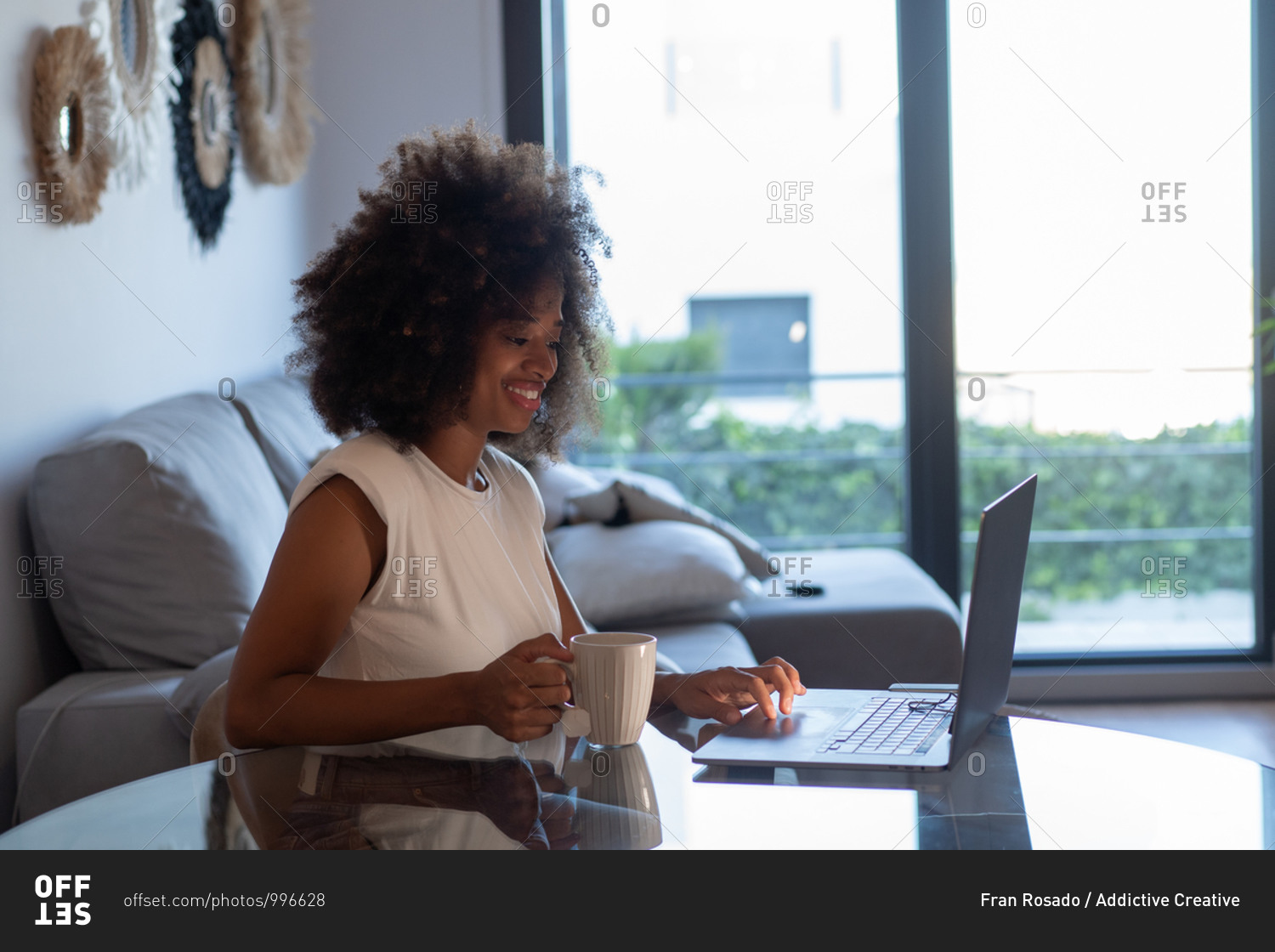 Concentrated African American female entrepreneur sitting at table with cup of tea and working on remote project while using netbook at home