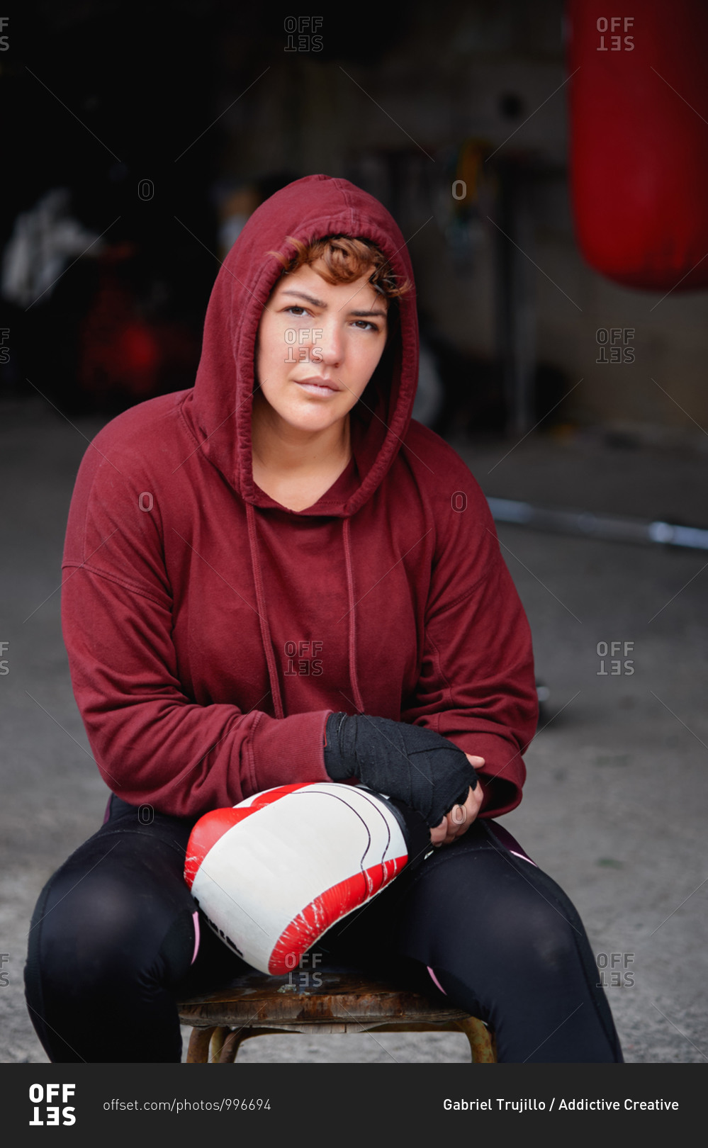 Concentrated female boxer in leggings and hoodie wrapping hands with black boxing wraps before boxing workout in shabby basement gym