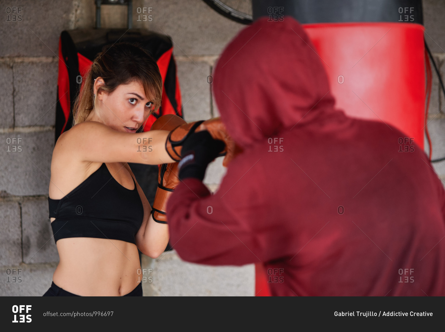 Full body sporty focused female fighters wearing sportswear and boxing gloves hitting punching bag during intense working out together in garage gym