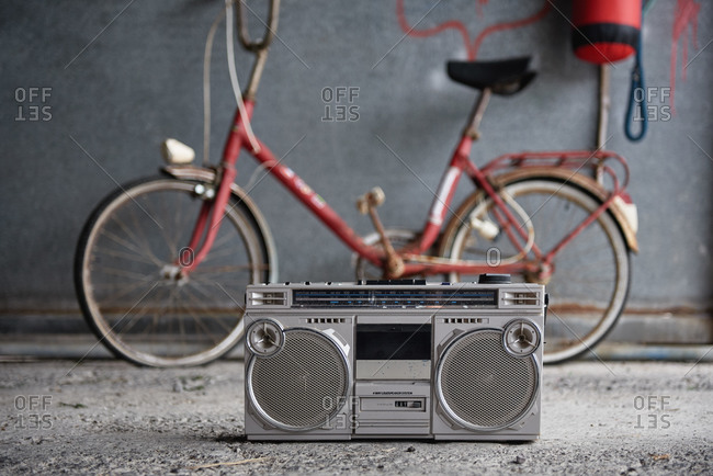 Old fashioned single cassette portable tape player placed on concrete floor against blurred red bicycle and gray shabby wall in garage