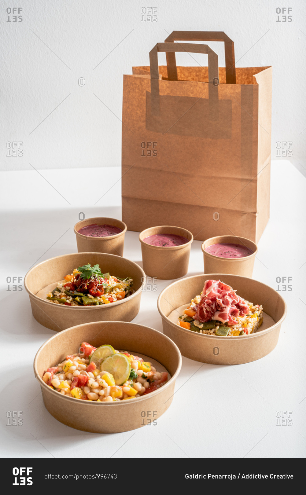 From above Molí de Pals vegetable rice, iberico ham and Shrimp Ceviche in carton bowls placed on paper bag on table with delicious beetroot cream