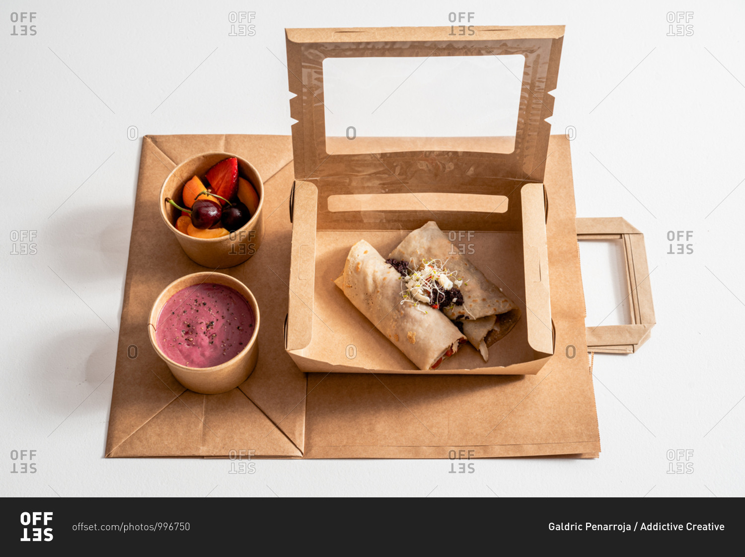 From above of delicious buckwheat crepe with roasted vegetables in carton container arranged with beetroot cream and ripe fruits in bowls on table