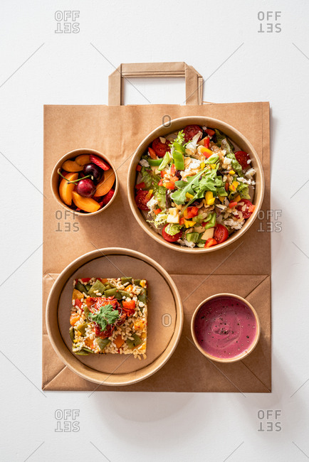 Top view of palatable vegetable salad with various nutritious ingredients in cardboard bowl placed on paper bag near rice with Molí de Pals vegetable rice and beetroot cream and fruit bowl