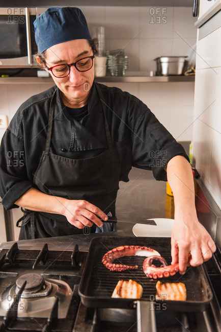Female chef in glasses grilling octopus and bacon