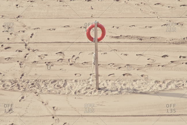 High angle of red lifesaver placed on wooden pole on sandy beach with various footprints