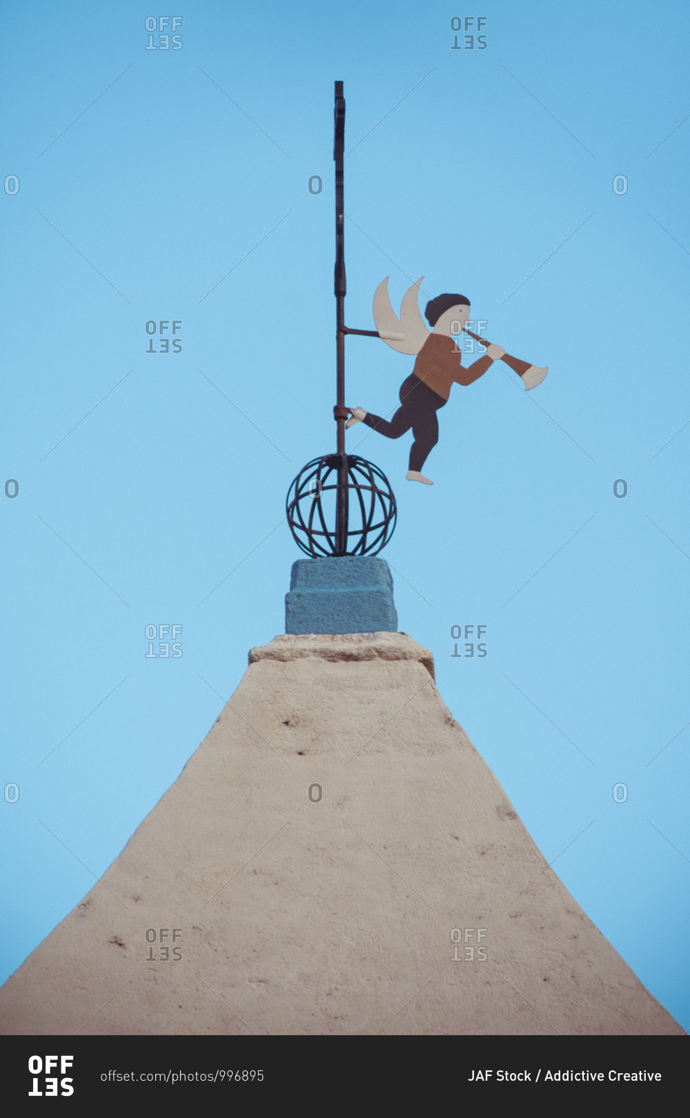 From below of weather vane in shape of little angle playing musical instrument on cross of temple dome under blue sky