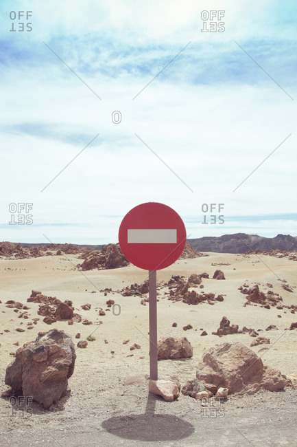 Prohibitory round red no entry road sign with white rectangle across placed on rural sandy desert terrain on hot day one way traffic