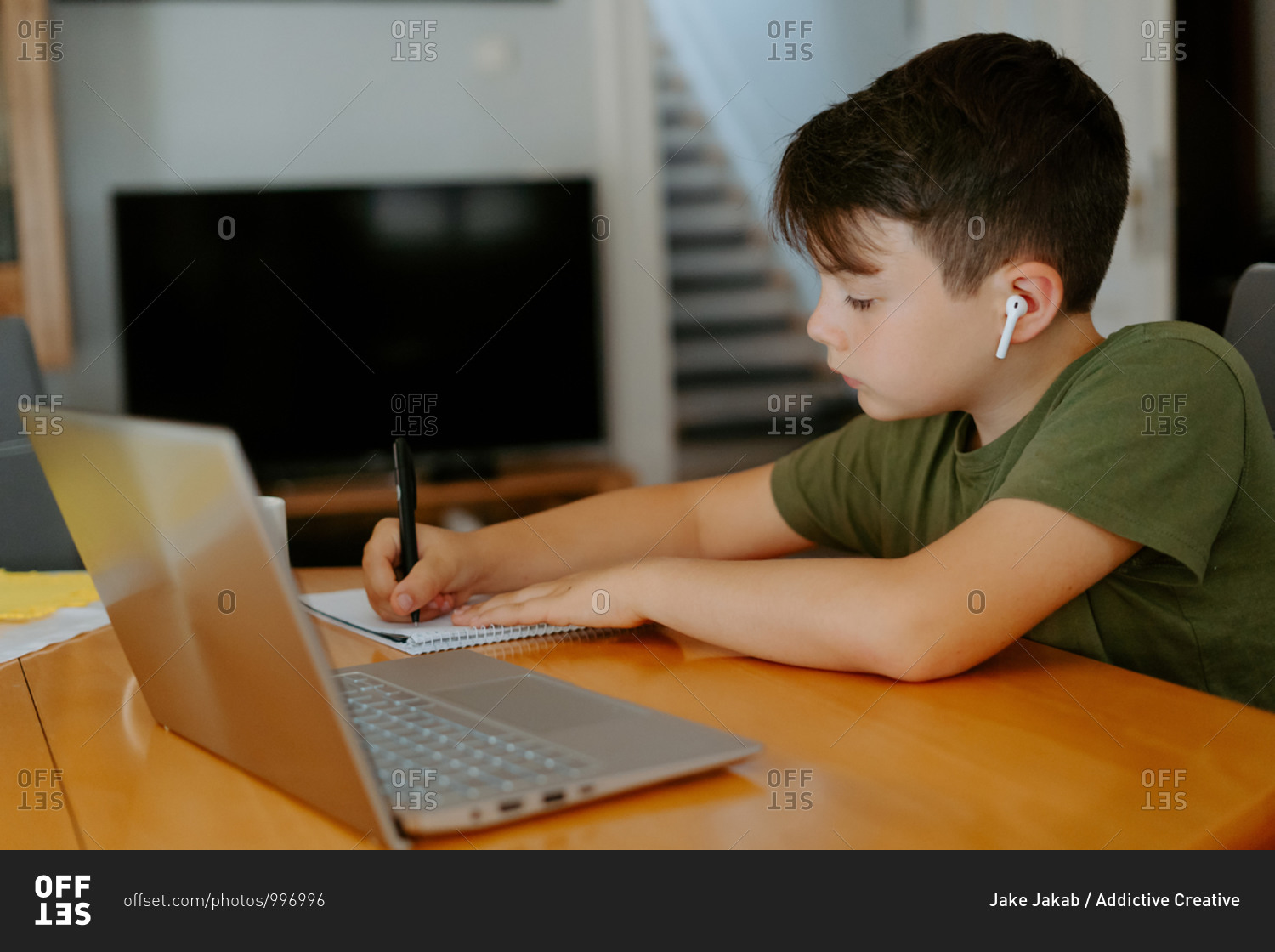 Side view of child writing in spiral notebook while doing homework assignment at table with cup of hot drink