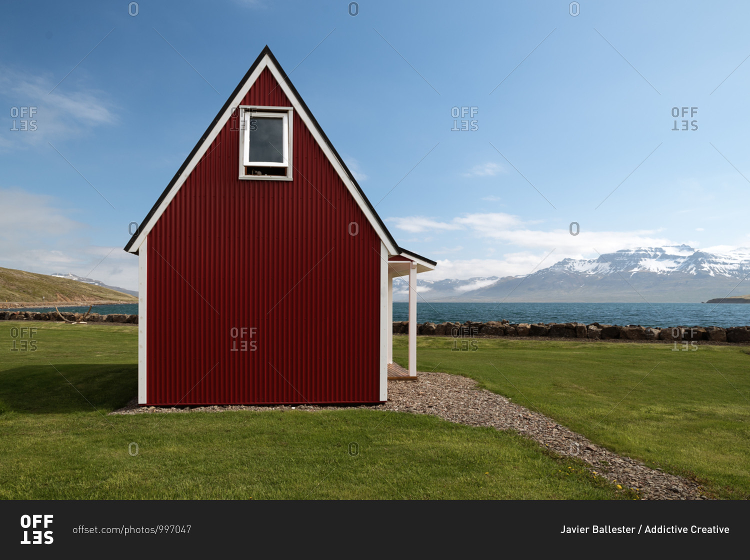 Small wooden cabin located on green lawn on background of lake and mountain ridge on sunny day under blue sky