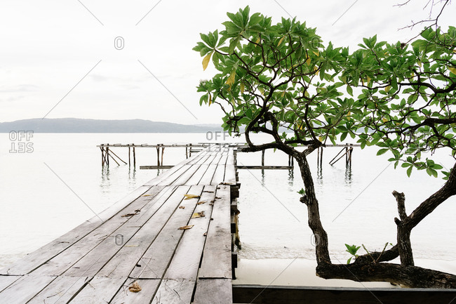 Shabby wooden quay in clean water of pond on background of mountains on overcast day