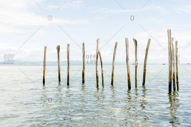 Shabby wooden poles placed in clear water of sea on sunny day on background of blue sky
