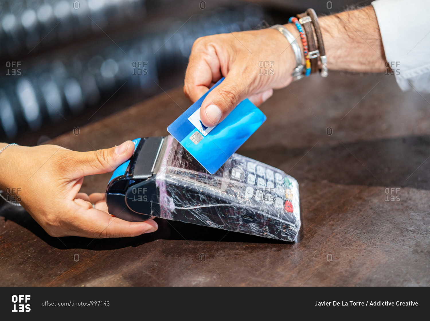 Cropped unrecognizable person standing at counter helping client to pay using POS machine and credit card working in cafe