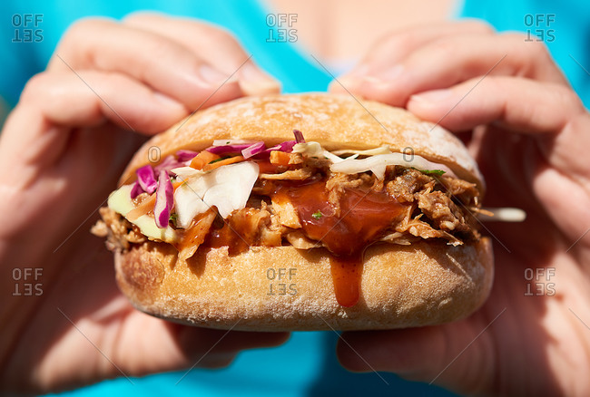 Anonymous woman holding messy pulled pork sandwich on a bun