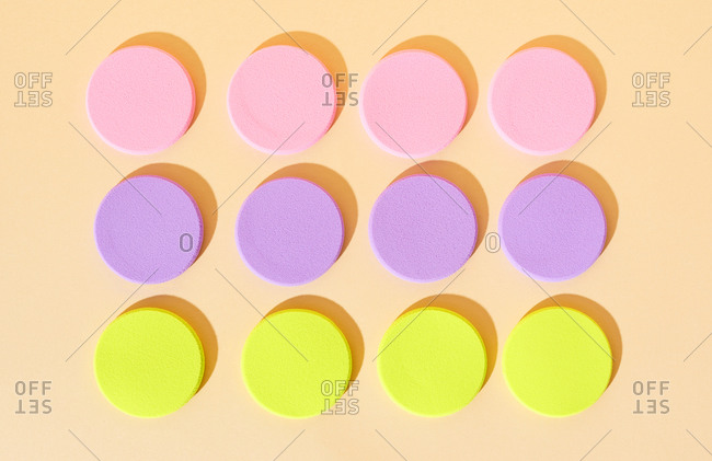 Round colorful makeup sponges arranged on neutral background